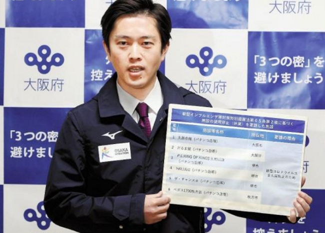大阪府知事吉村洋文在記者發布會上，親自舉牌曝光不顧政府請求、仍然強行營業的老虎機廳。圖片來源：讀賣新聞
